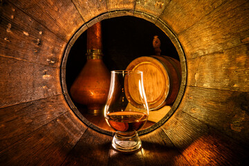A glass of whiskey in old oak barrel. Copper alambic on background. Traditional alcohol distillery...