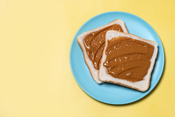 Bread toast with peanut butter cream on yellow background. Top view. Copy space