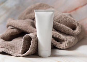 White blank squeeze cream tube near brown bath towel closeup, cosmetic mockup. Handmade cosmetic