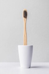 Sleek bamboo toothbrush stands upright in minimalistic white hol