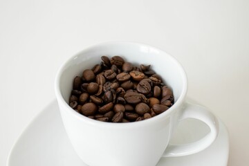 Close-up of a white cup filled with roasted coffee beans on a white saucer
