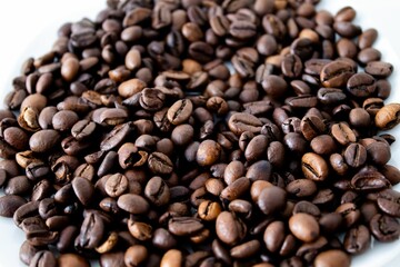 Fototapeta premium Close-up of roasted coffee beans on a white surface, showcasing rich textures and hues.