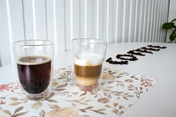 Glass cups of coffee on a floral mat with coffee beans spelling 'coffee' in a bright modern setting