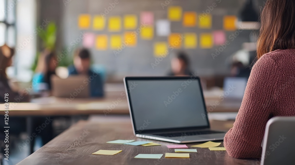 Poster a person sits at a desk with a laptop and sticky notes, while others collaborate in a modern workspa