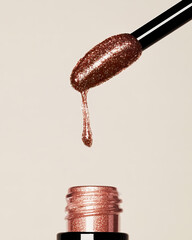 A shimmering rose-gold glitter lip gloss drips from a sleek applicator above its elegant black bottle, capturing the essence of luxury and beauty on a soft beige background