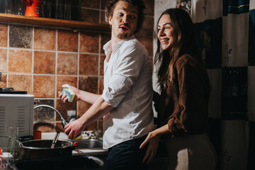 A young couple shares playful and joyful interactions while doing household chores in a warm kitchen. The setting conveys domesticity, love, and a serene atmosphere in their collaborative activity.
