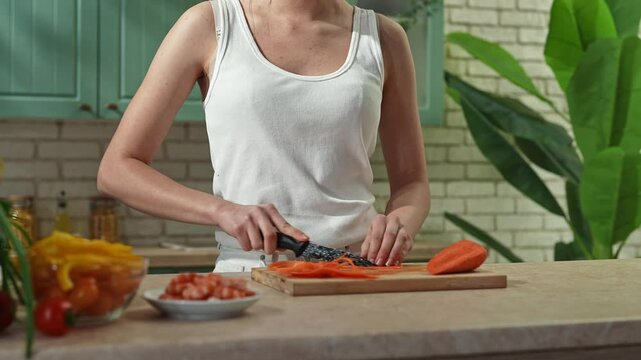 Young woman at the table in the kitchen preparing spring rolls for healthy lunch, woman cutting carrot with knife on slices. Slow motion.