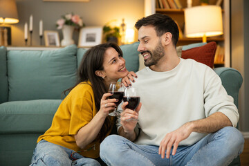 A laughing couple enjoying wine together, embracing a cozy atmosphere filled with love and happiness in their home.