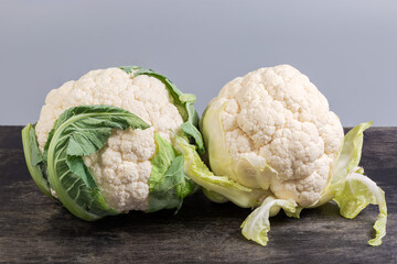 Two whole raw cauliflower heads on black surface, front view