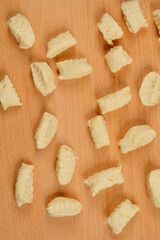 A top-down view of irregularly shaped cheese and flour gnocchi pieces scattered on a wooden cutting board, ready for cooking