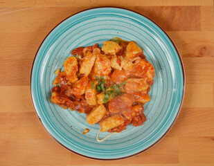 A top-down view of cheese and flour gnocchi in tomato sauce with mozzarella on a blue plate, placed on a wooden surface