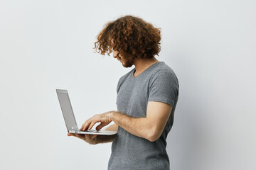 Young man with curly hair using a laptop, showcasing tech savvy attitude in a minimalist setting,...