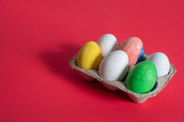 Colorful painted Easter eggs in a cardboard box on a red background.