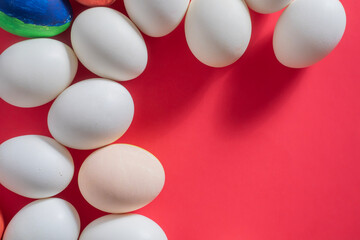 White and colorful eggs arranged on a vibrant red background, perfect for Easter.