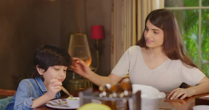 Indian family group sitting around dining table chair enjoy night dinner indoor home. happy adult dad male man young woman cute teen girl child talk eat tasty food fresh salad spend time have fun joy