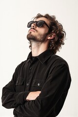 Fototapeta premium Portrait of a young man with curly hair, beard, and sunglasses, wearing a black shirt, against a white background.