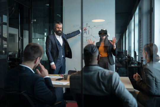 Business team in a modern office during a presentation on artificial intelligence. A woman in a VR headset interacts with a virtual environment. Concept of innovation and future technology
