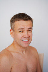 Naklejka premium Portrait of a smiling middle-aged man with a naked torso on a white background. photo posing. men's physical and mental health 
