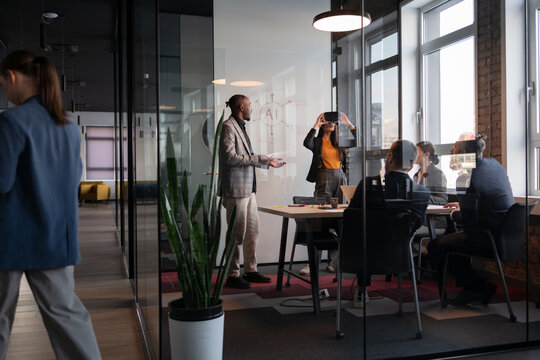 Diverse business team in a modern office discussing AI technology. A woman wearing a VR headset explores virtual reality, while colleagues engage in conversation. Concept of innovation and teamwork - Powered by Adobe