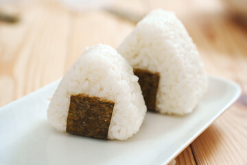 Onigiri made of rice and nori seaweed are spun on a white plate. A simple and delicious Asian snack meal.