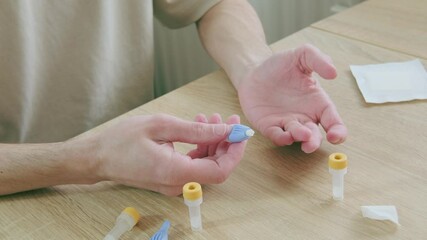 Male fingers closeup, man performing self-administered medical test pricking finger and collecting blood in tube, fingertips Personal health data, rapid diagnostic at-home test
