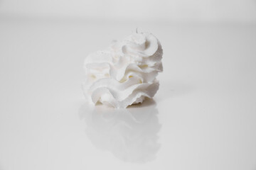 Whipped milk cream from the tube is squeezed onto a white surface. A delicious milk dessert.