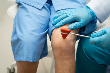 Asian doctor knock on knee reflex nerve for check and treatment senior patient in hospital.