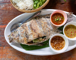 Pla Pao, Thai grilled fish with salt, served with chili sauces, vegetables and rice noodles. Filled with lemongrass, cilantro and other herbs