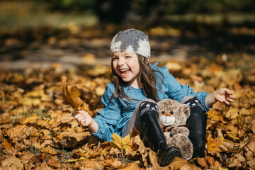 A stylishly dressed little girl plays in an autumn park with a plush toy. The concept of style, comfort, and childhood joy in warm autumn moments.