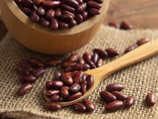 Fototapeta premium Red kidney beans in a scoop on a wooden table against a white background.