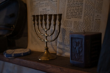 A brass menorah stands on a wooden shelf against a backdrop of Hebrew texts, symbolizing Jewish...