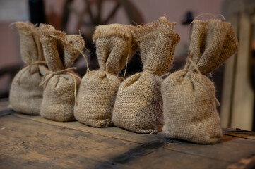 A row of small burlap sacks tied with twine, arranged on a rustic wooden surface, evoking a sense of vintage agriculture, traditional packaging, or organic storage.