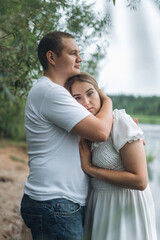 Fototapeta premium Romantic couple kissing and embracing near a lake and forest on a cloudy day.