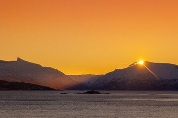 A beautiful sun shining over the snowy mountains and fjord during the first day of arctic winter. Arctic nature in Scandinavia during winter season.