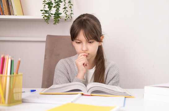 Girl is doing her homework at her desk and is worried, biting her nails, nervous and very anxious. An excited child is nervous under stress.