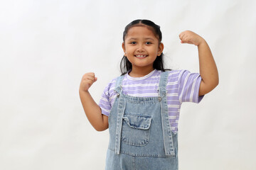 Happy asian little girl standing while showing strong hand gesture. Isolated on white background
