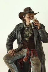 Portrait of man, cowboy in leather coat, hat, jeans and shirt drinking dark foamy beer against...