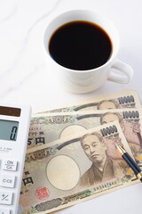 福沢諭吉の肖像の一万円紙幣と電卓、淹れたてのコーヒー
