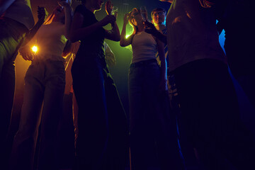 Group of energetic young people, boys and girls, enjoying lively party in a dimly-lit night club with neon lights. Spirit of youth culture and entertainment. Concept of leisure, celebration, enjoyment