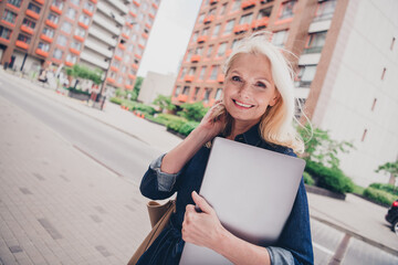 Charming mature woman with blonde hair smiling in casual denim while enjoying a sunny city walk