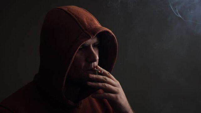 A man smokes a cigarette. Craving for smoking. A cigarette on a black background, smoke is visible. A lot of noxious smoke. Experienced smoker. This is bad for your health. Problems and depression