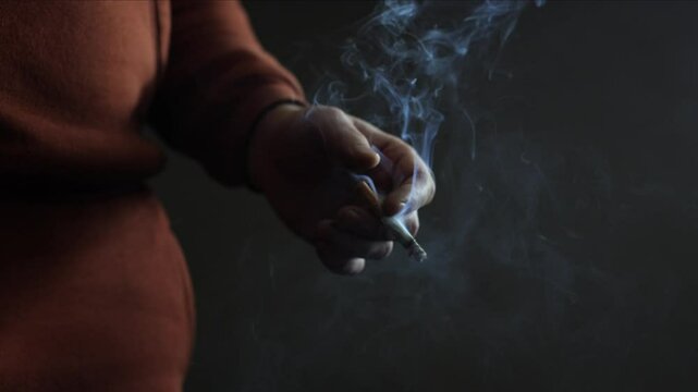 A man smokes a cigarette. Craving for smoking. A cigarette on a black background, smoke is visible. A lot of noxious smoke. Experienced smoker. This is bad for your health. Problems and depression