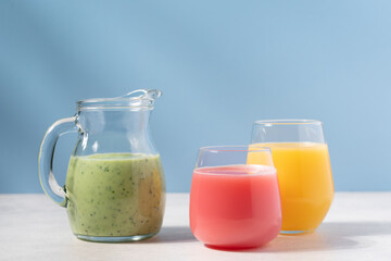 Green, red and orange smoothies on blue background. Vitamin drinks side view