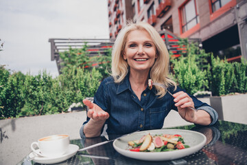 Charming elderly woman enjoying lunch outdoors in a lively city setting with denim style