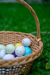 Wicker basket overflowing with colorful decorated easter eggs on green grass