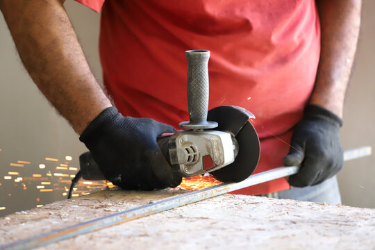 
Close-up of worker's hands cutting metal and removing sparks with electric grinder