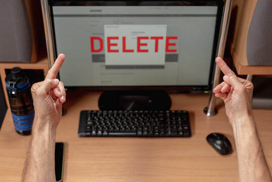 Rude angry man showing two middle fingers to computer screen with text delete, Male user reacting with anger as data deletion occurs on screen, account removal in progress