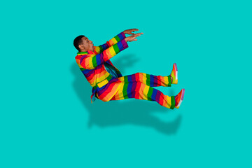 Young man in rainbow outfit posing against bright teal backdrop, expressing vibrant energy and...