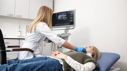 A doctor in blue gloves performs a thyroid ultrasound, moving the probe on a young patient’s...