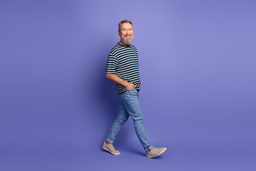 Fototapeta premium Stylish elderly man walking confidently wearing a striped t-shirt, standing against a vibrant purple background